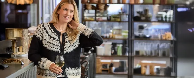 Woman wearing a white and blue cardigan holding a glass of white wine.