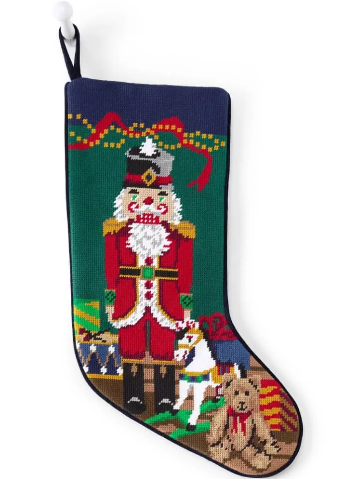 Needlepoint holiday stocking with the embroidered image of a nutcracker and children's gifts.
