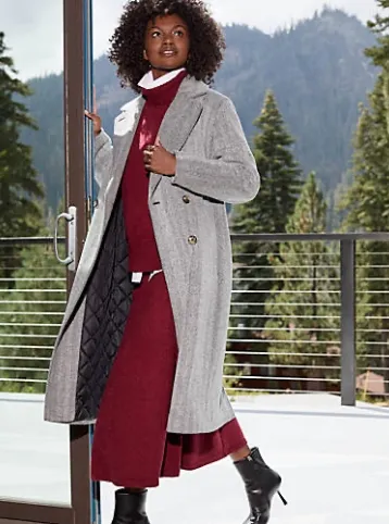 Woman wearing a maroon sweater and matching skirt under a gray wool trench coat.