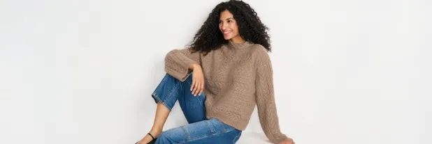 Woman wearing a brown sweater and cropped blue jeans.