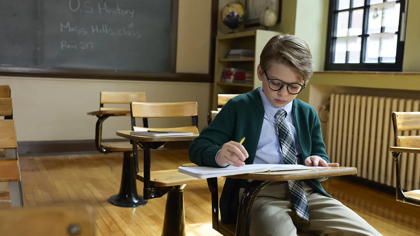 Boy sitting at a desk wearing a Lands' End school uniform.