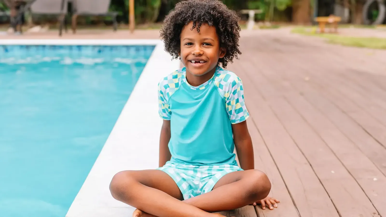 Boy wearing a turquoise checkered rashguard and matching swim shorts.