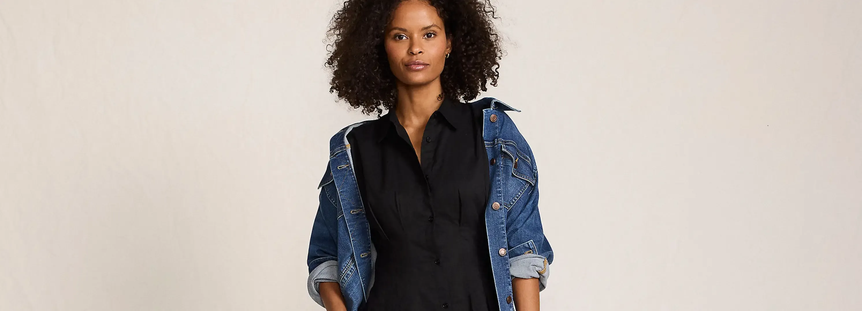 Woman wearing a denim jacket over black shirtdress.