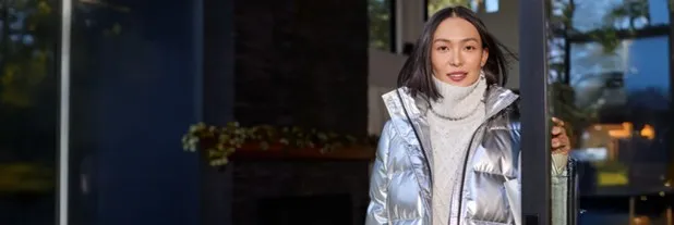 Woman wearing a white cable knit turtleneck sweater under a silver puffer jacket.