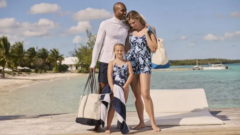 Family dressed in Lands' End swimwear, carrying beach totes and towels.