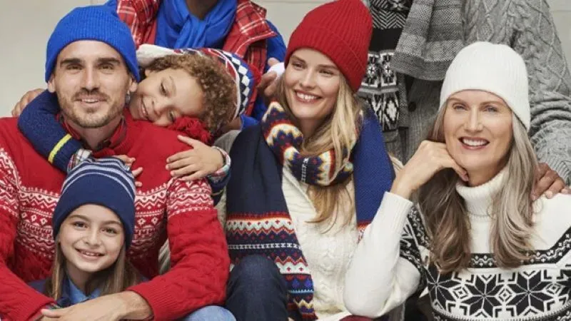 A family dressed in holiday sweaters and stocking caps poses for a photo.