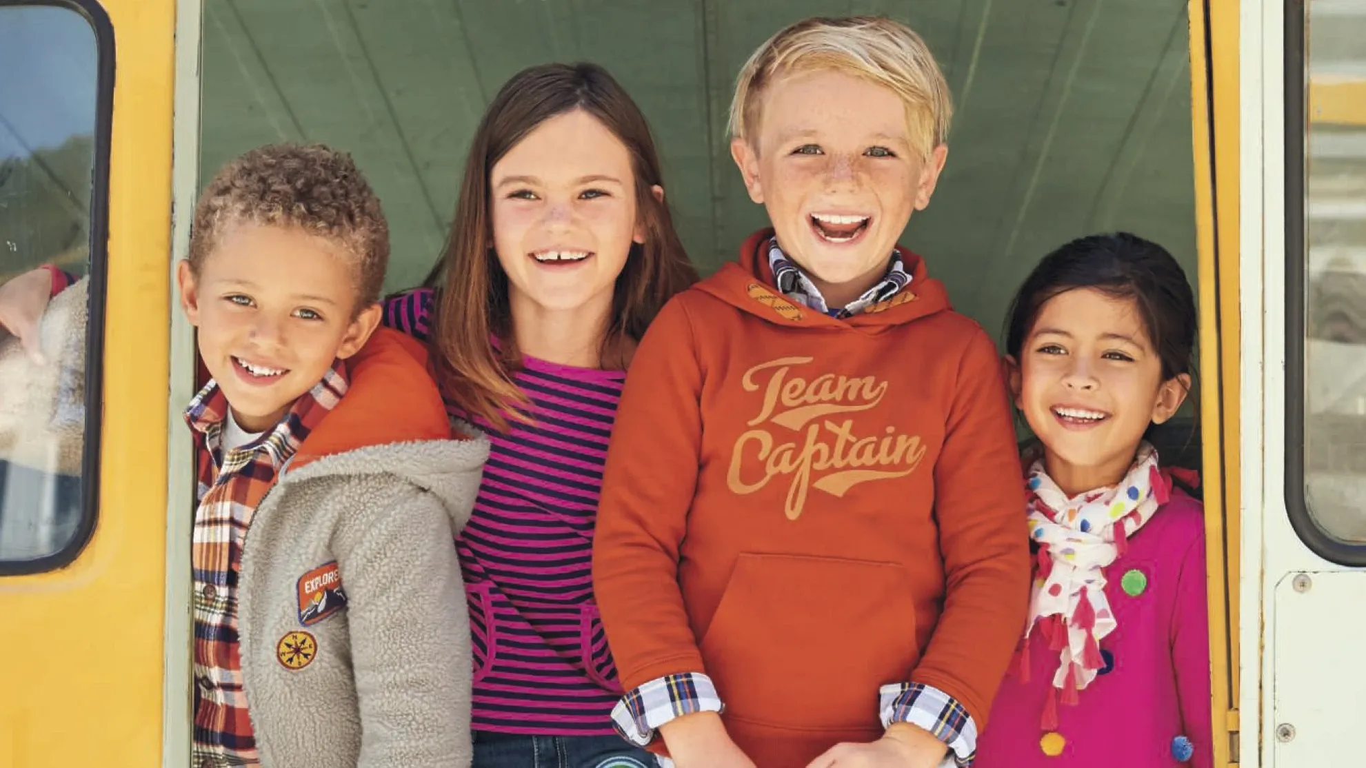 Four kids standing at the back door of a school bus.