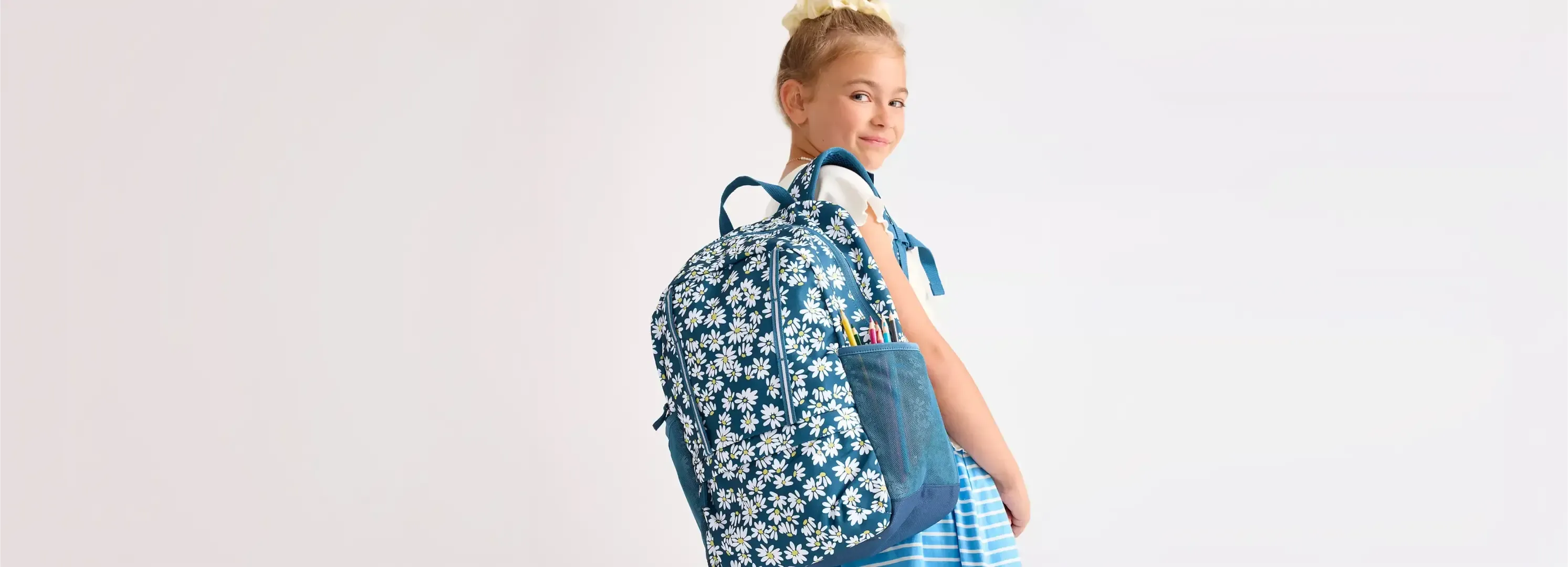 Girl wearing a blue daisy-print backpack.
