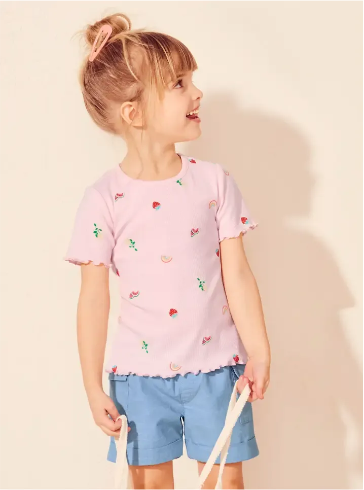 A young girl wearing a light pink T-shirt paired with blue shorts.