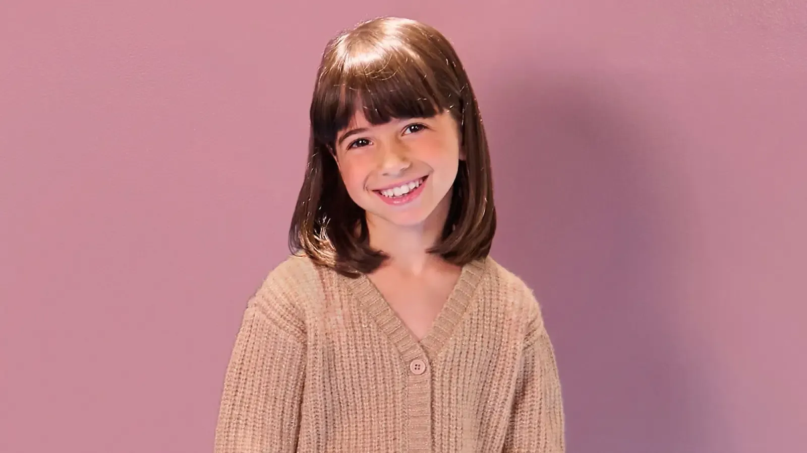 Young girl wearing a tan cardigan sweater.