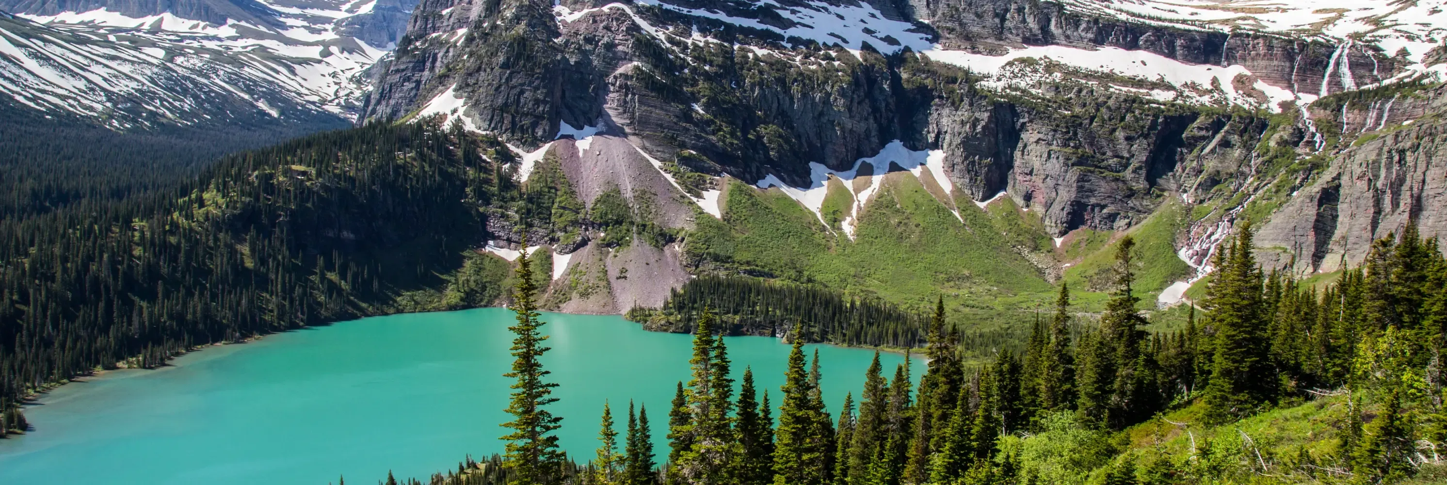 Turquoise alpine lake beneath snowy cliffs.