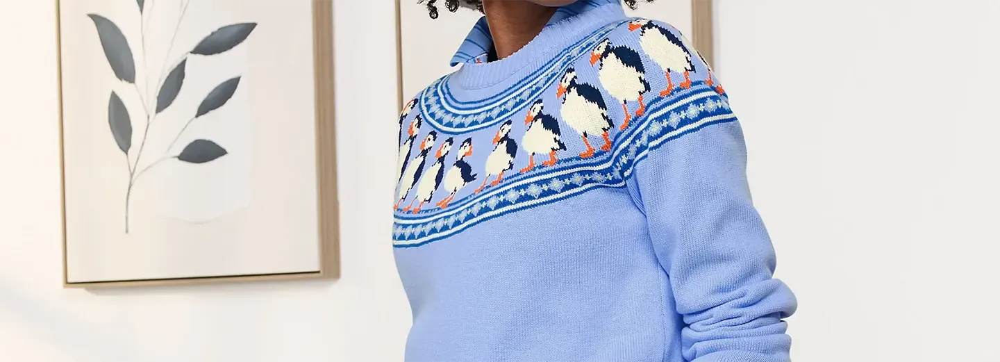 Woman wearing a light blue puffin fair isle sweater over a collared shirt.