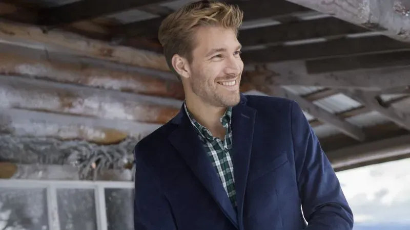 Man wearing a blue suit coat over a green and white plaid shirt.