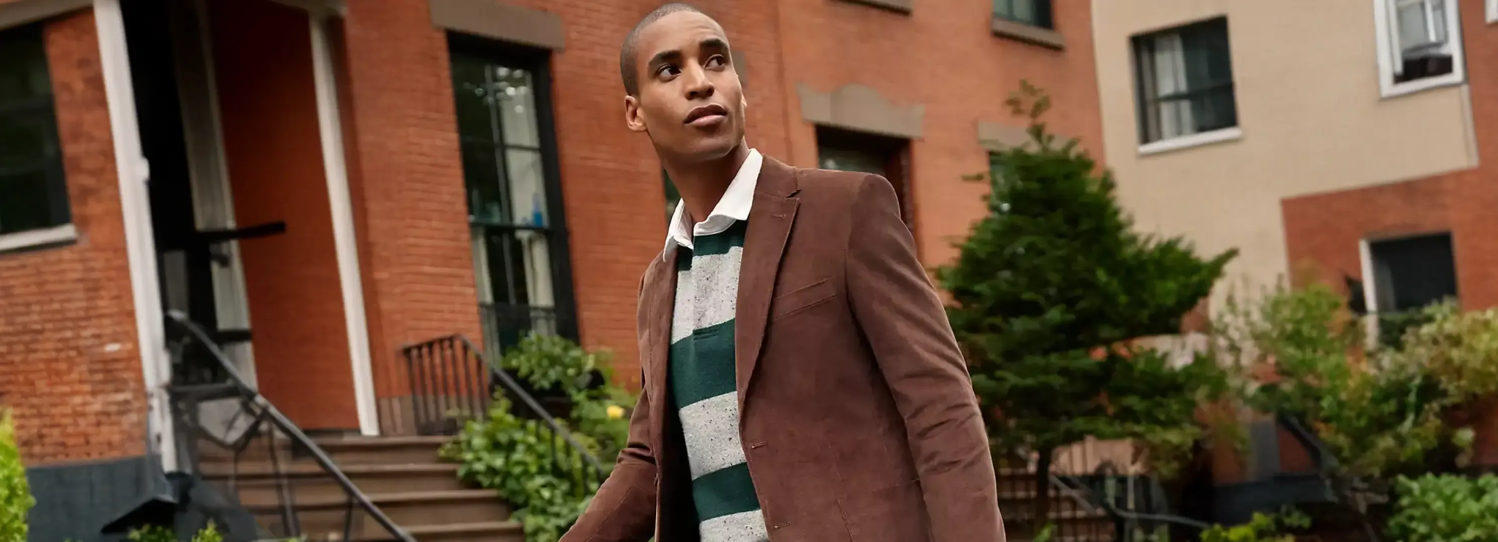 Man wearing a brown blazer over a green and grey striped polo