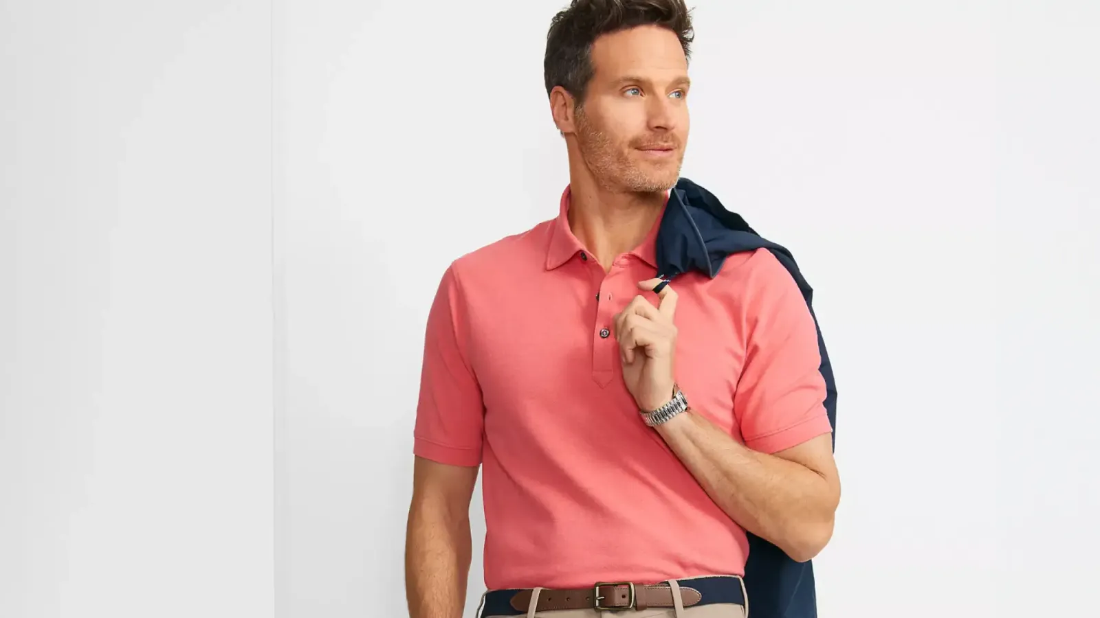Man wearing a coral polo shirt and a jacket over his shoulder.