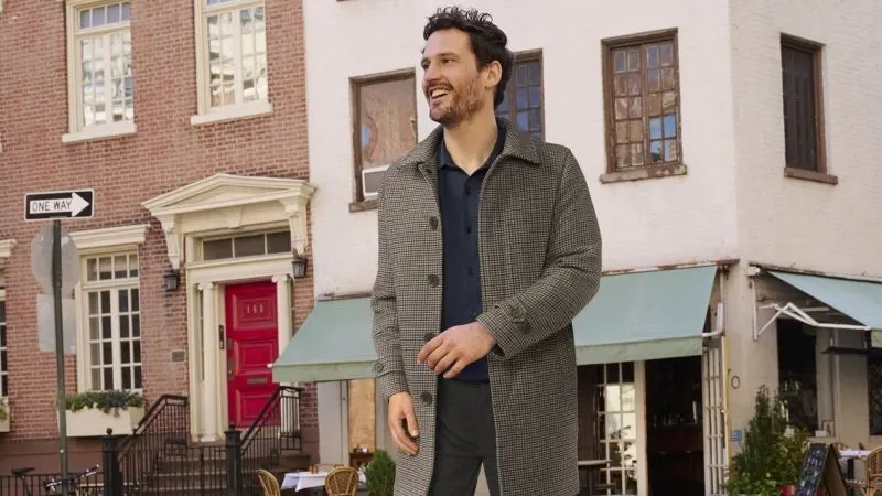 Man wearing a gray wool overcoat over a navy blue button down shirt in an urban setting.