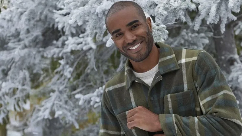 Man wearing a green plaid fleece shirt jacket near snow covered trees.