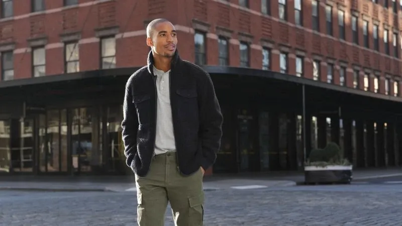 Man wearing a light-weight fleece jacket standing in a city street.