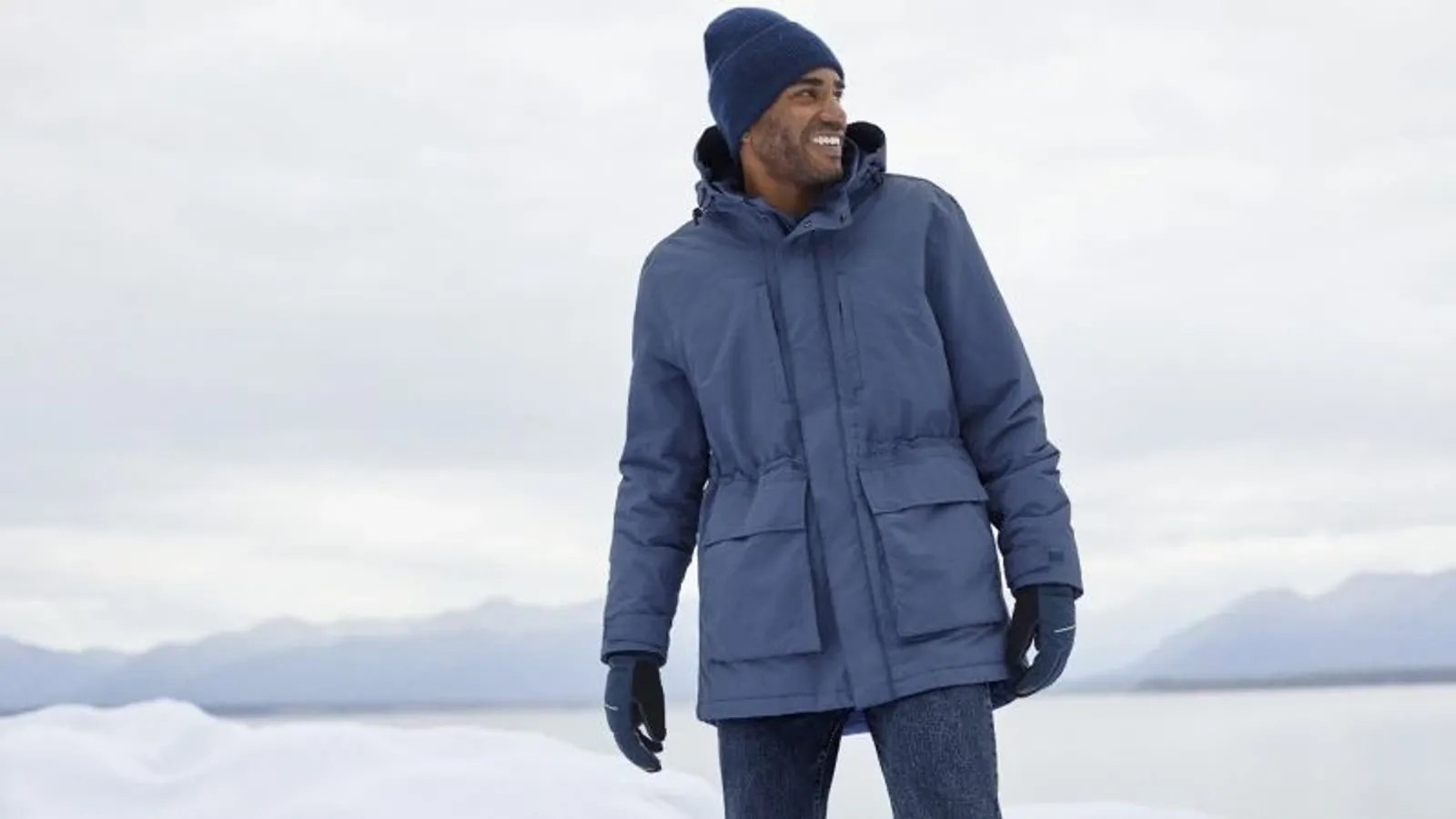 Man wearing a navy-blue squall parka with matching hat and gloves in a snowy outdoor landscape.