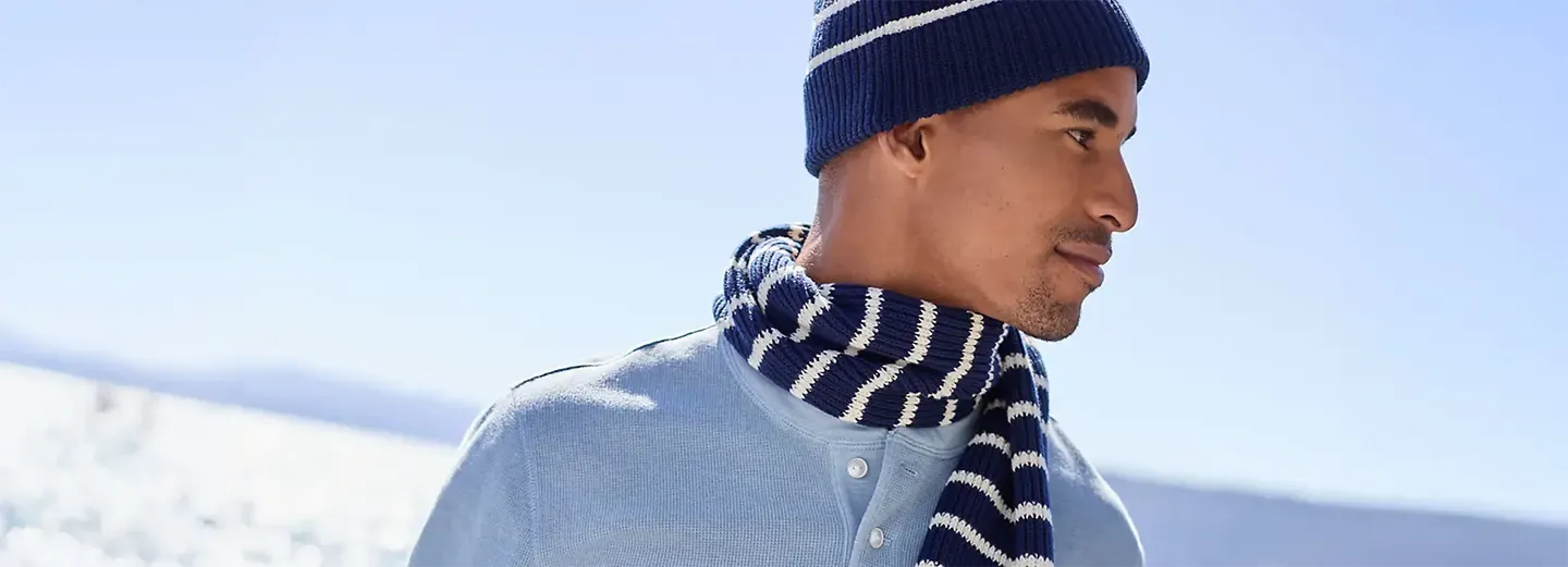 Man in navy blue and white striped scarf and beanie, and a light blue henley shirt outdoors.