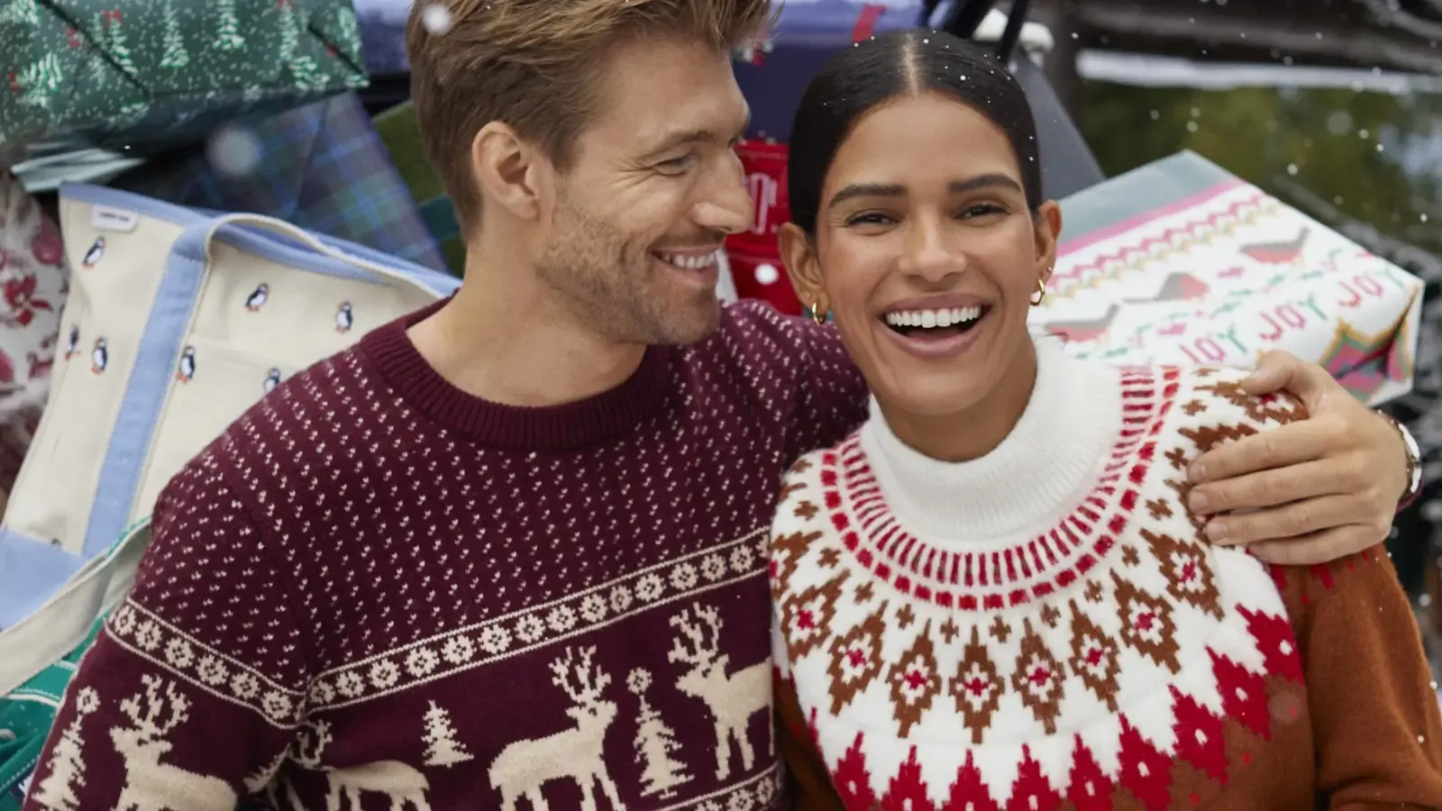 A man and woman embrace while wearing festive Christmas sweaters.