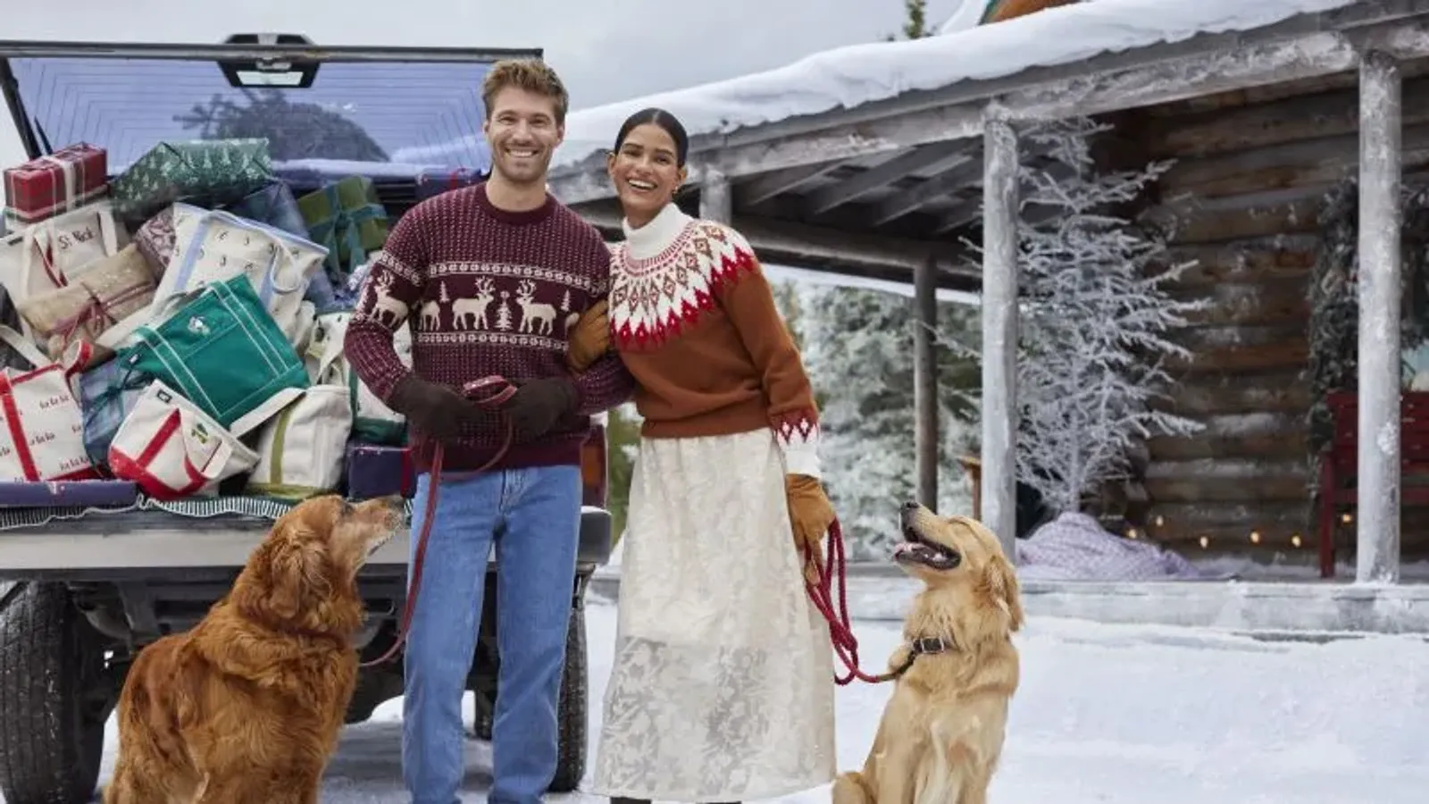 A man and woman stand with their two golden retrievers in front of an SUV overflowing with gifts and Lands' End tote bags.