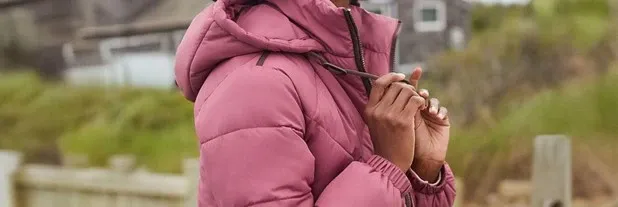 A person pulls on the hood strings of a pink, hooded puffer jacket.
