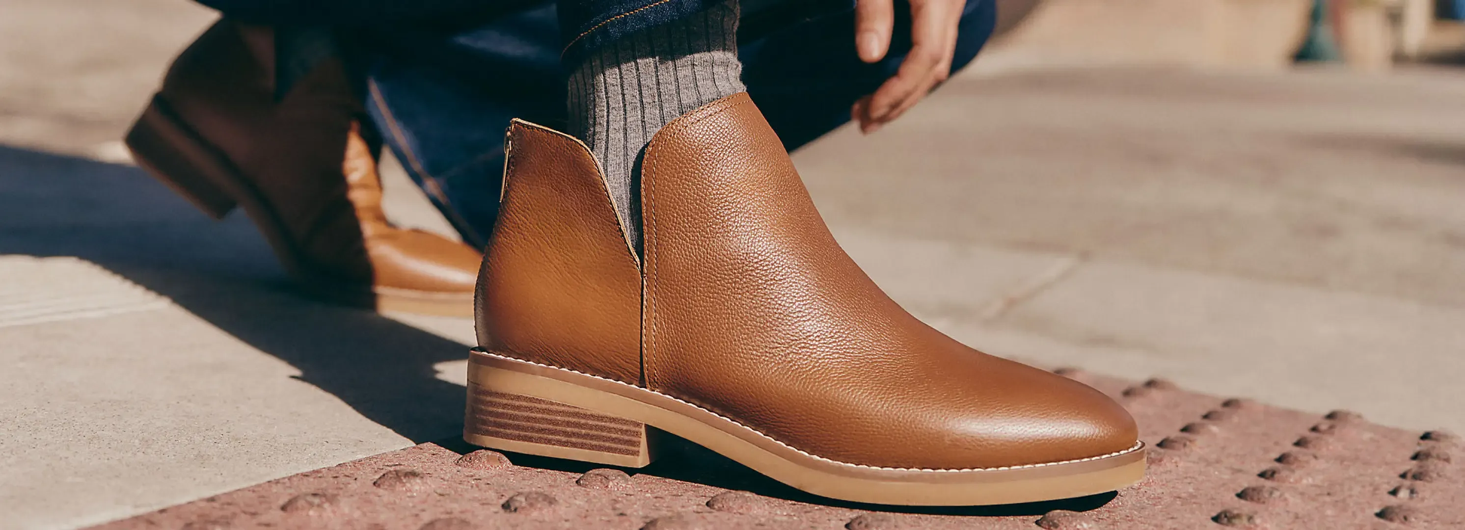 Close-up tan leather ankle boots with ribbed socks on sidewalk