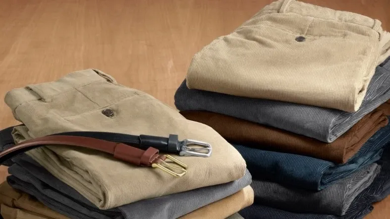 Ten folded and stacked pairs of dark and neutral colored Lands' End corduroy pants and two leather belts.