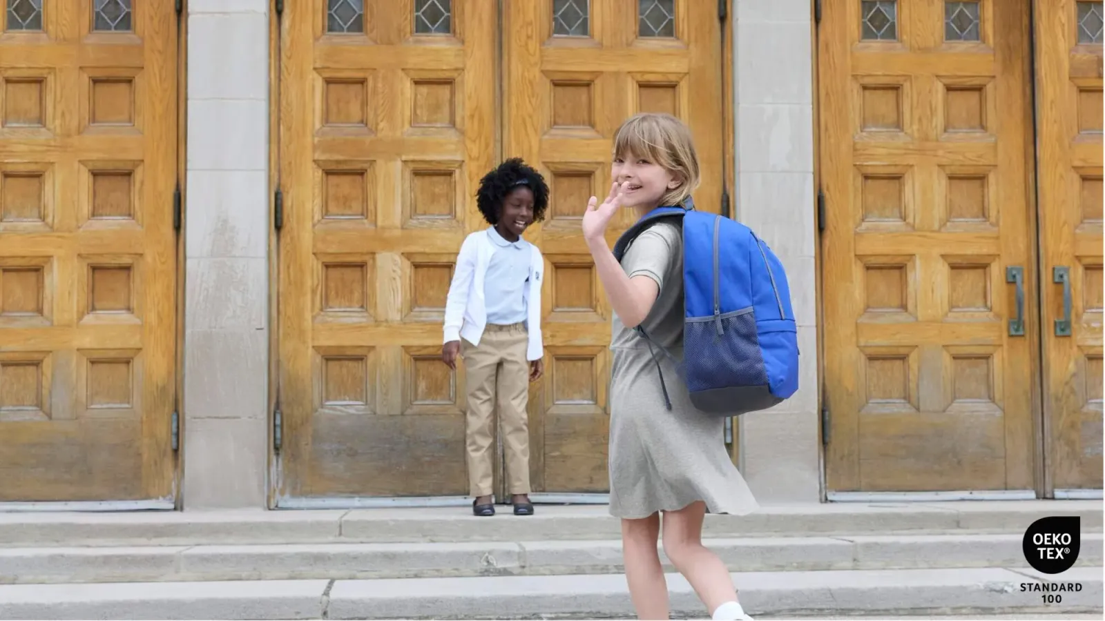 Two girls wearing school uniforms in front of large wooden doors.
