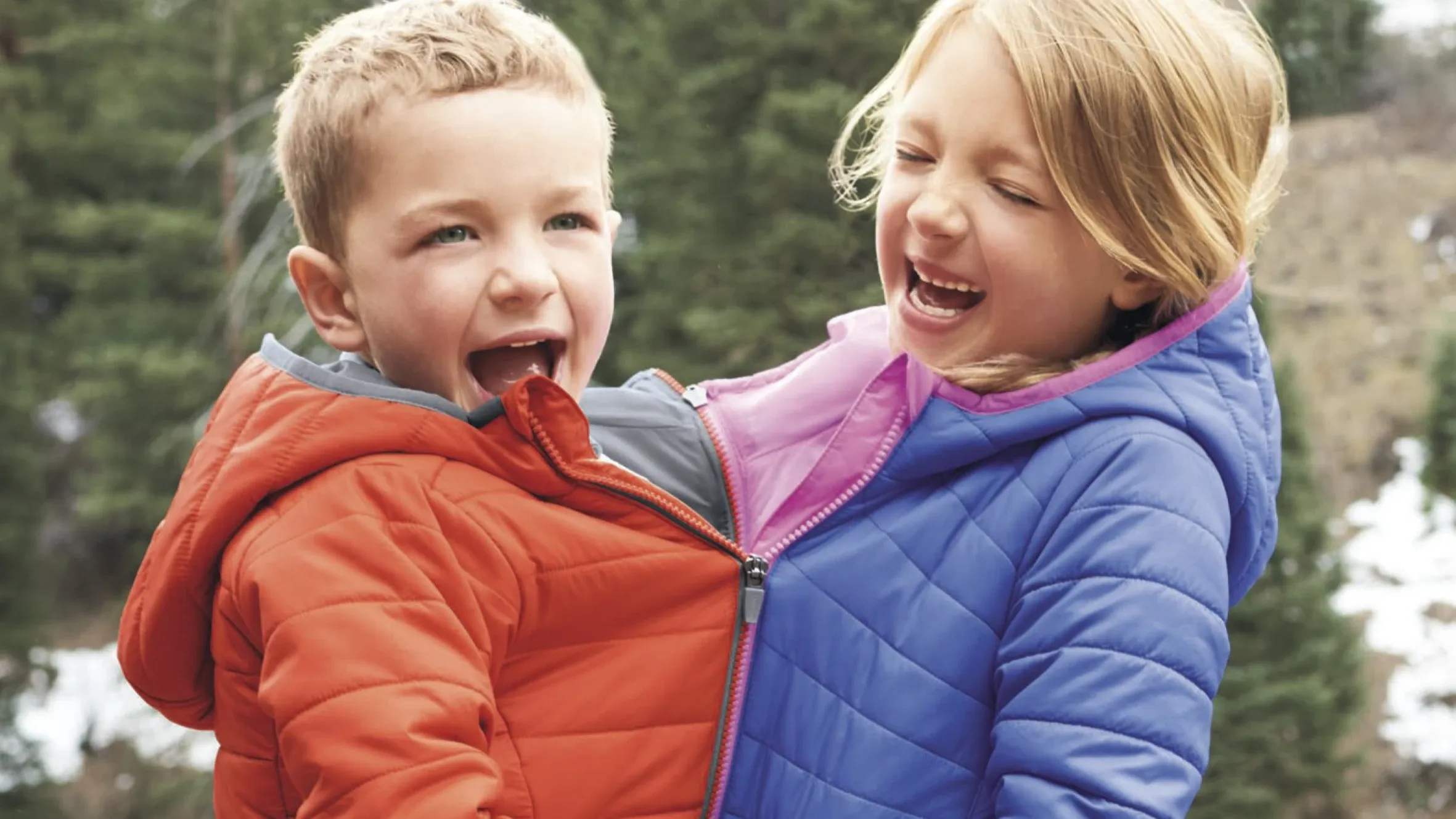 Two kids with their puffer jackets zipped together.