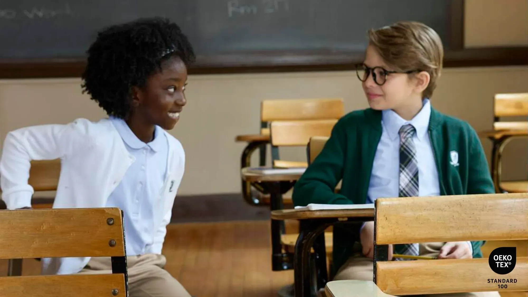 Two students wearing Lands' End school uniform shirts and sweaters sit at desks in a classroom.