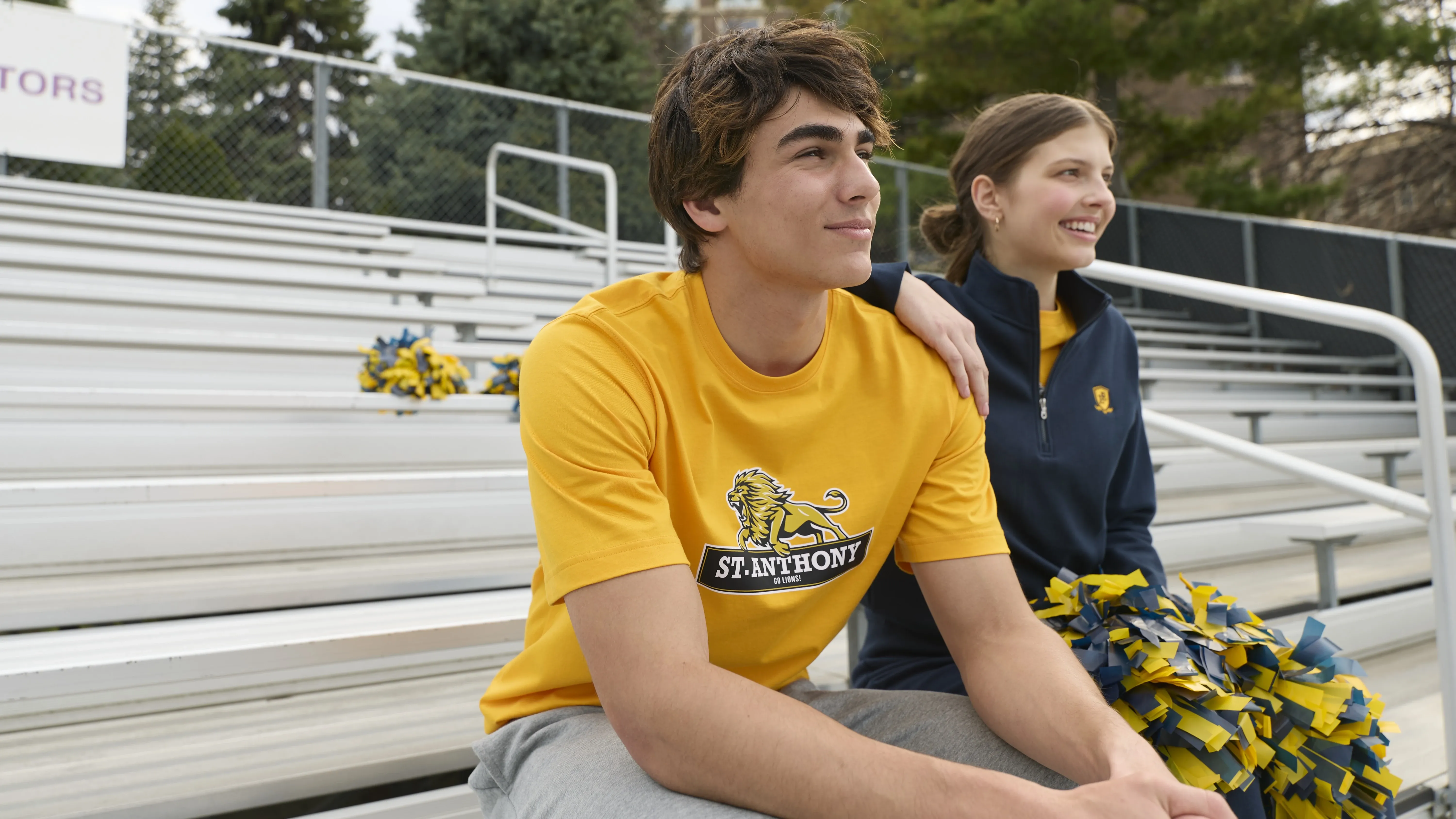 Two teenagers wearing school colors sitting on bleachers.