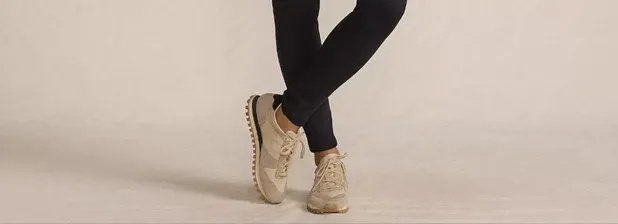 Woman wearing black leggings and beige sneakers.