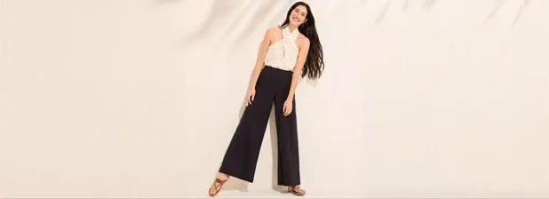 Woman wearing black Starfish high rise palazzo pants, ivory halter top and brown sandals.