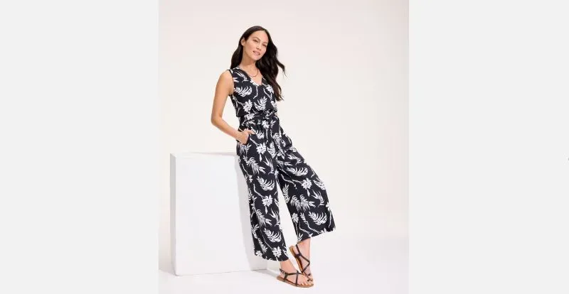 Woman wearing black and white floral jumpsuit and strappy sandals.