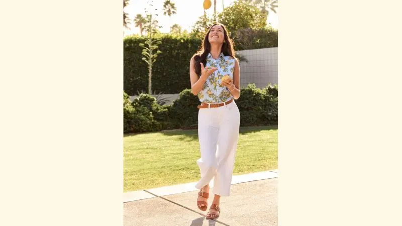 Woman wearing a blue and lemon sleeveless top, white cropped pants, brown belt and sandals.