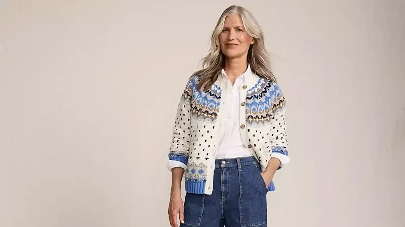 Woman wearing white and blue fair isle cardigan sweater over a button-down shirt and blue jeans. 