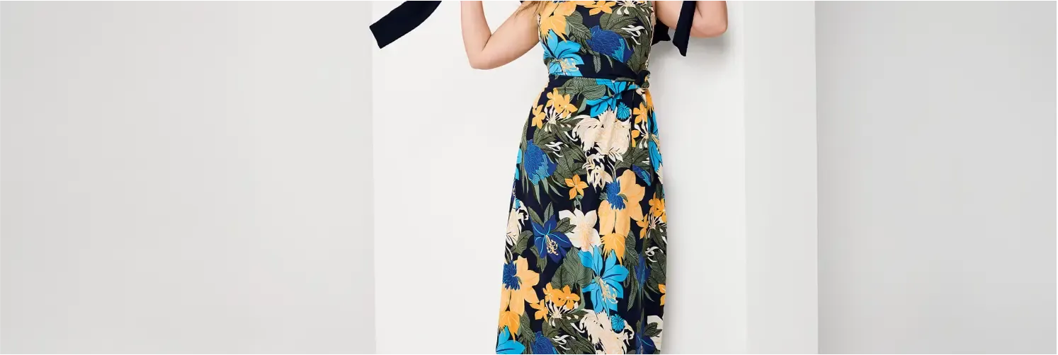 Woman wearing a sleeveless maxi dress with a blue, green, yellow and white floral pattern.