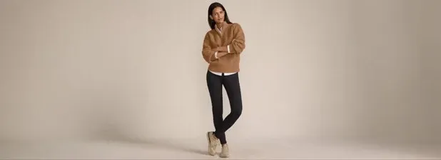 Woman wearing a camel quarter zip sweater over a white shirt and black leggings.