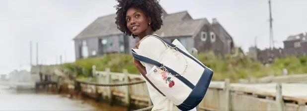 Woman carrying a canvas Lands' End tote bag with navy trim and a decorative charm.