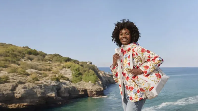 Woman wearing a jacket with white and red floral pattern, carrying a matching tote bag.