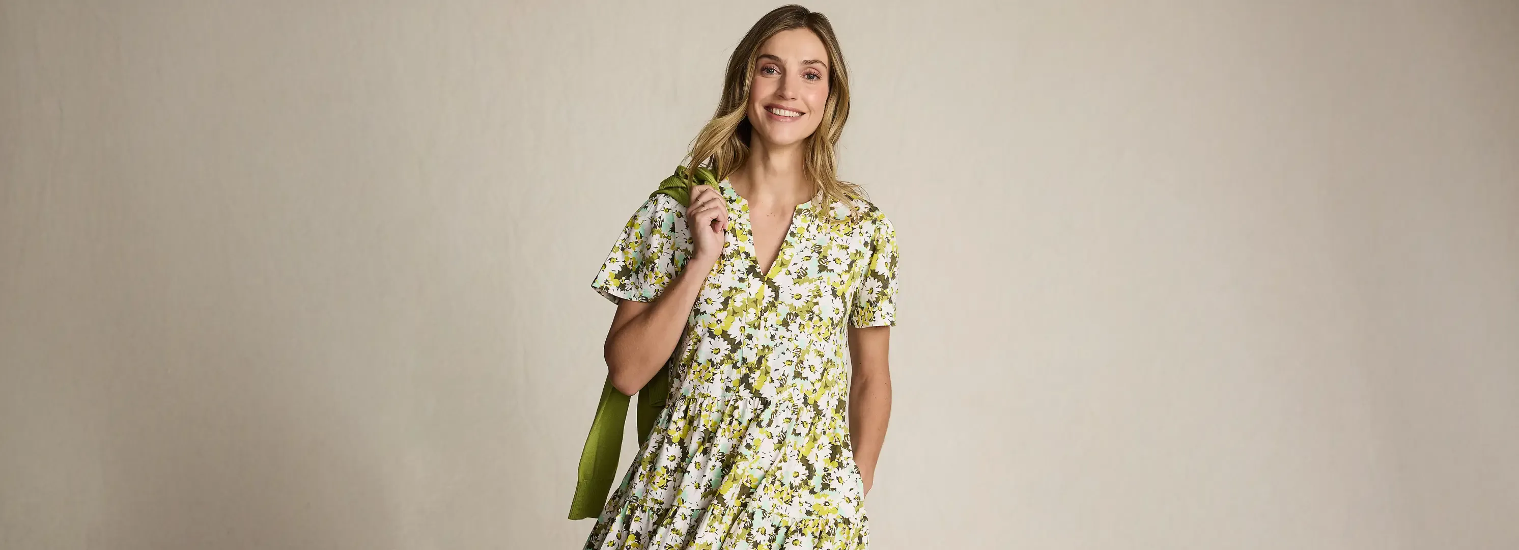 Woman wearing a floral tiered dress with green sweater slung over her shoulder.