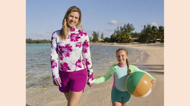 Woman and girl wearing long sleeve rashguards and board shorts.