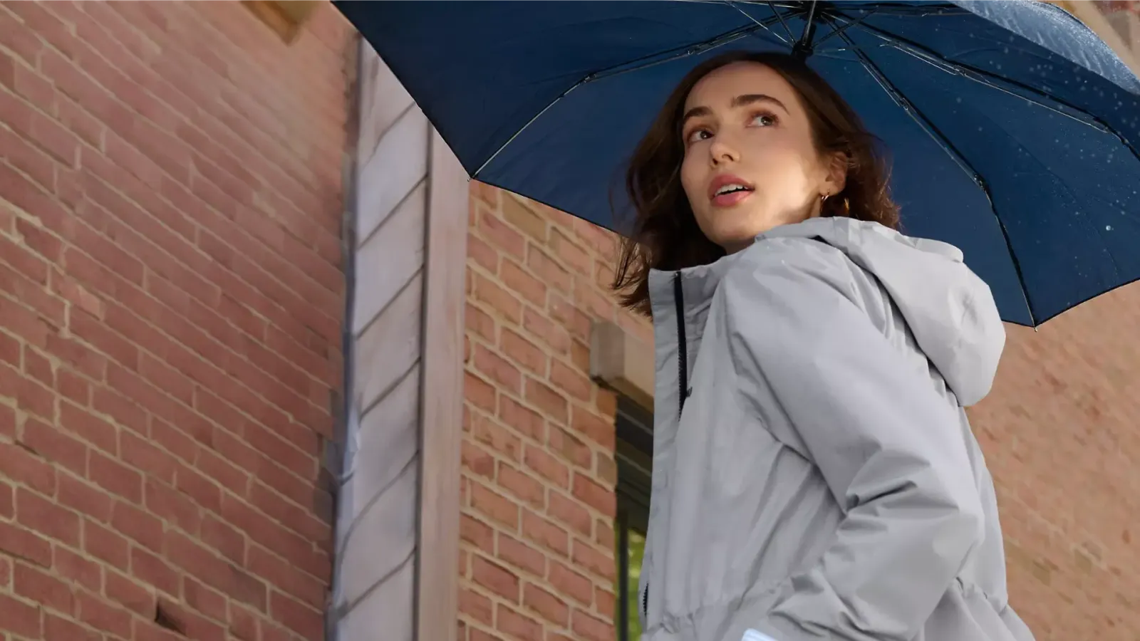 Woman wearing a grey coat holding a blue umbrella.