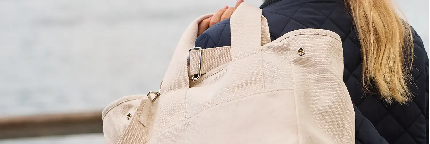 Woman wearing a navy blue quilted jacket, carrying a large beige canvas tote bag.