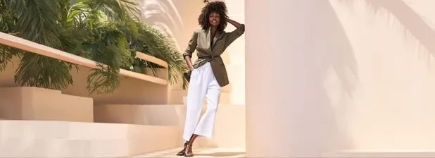 Woman wearing an olive belted jacket and white pants.