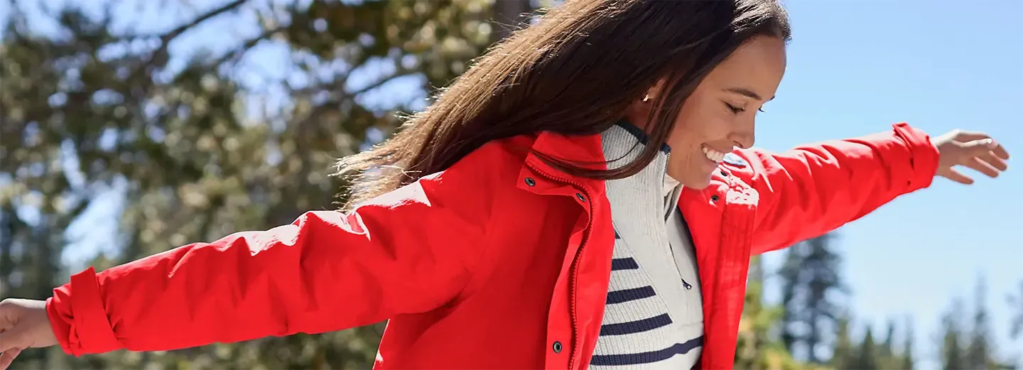 Woman wearing a red ski jacket over a striped knit sweater outdoors.