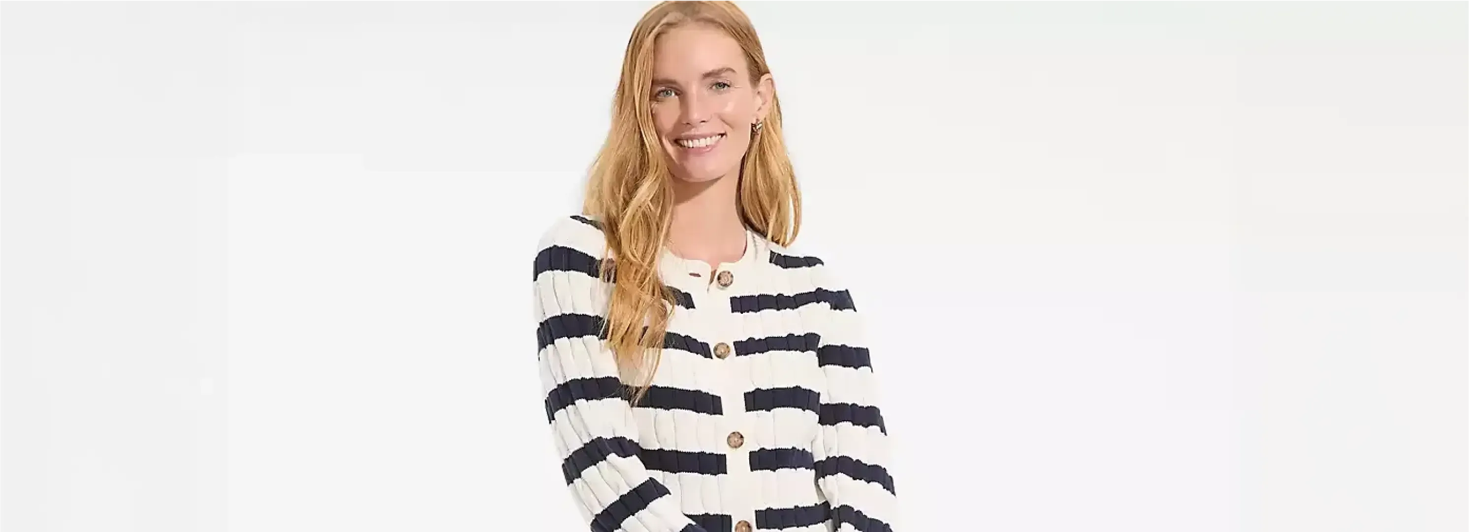 Woman wearing a striped cardigan holding a tote bag.