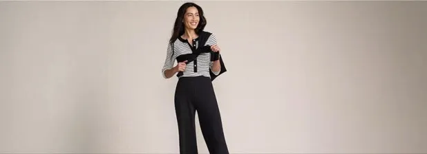 Woman wearing a striped top, a black sweater over her shoulders and black pants.